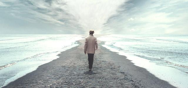 Man walking on a sand bar between two bodies of water